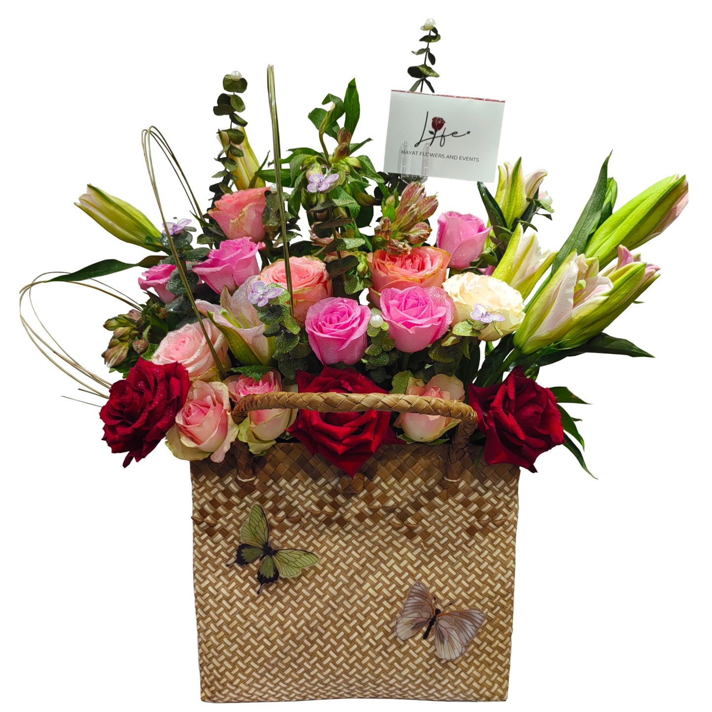 Floral arrangement in a woven basket with pink, red, and white roses and pink lilies, accented with eucalyptus baby blue and steel grasses.