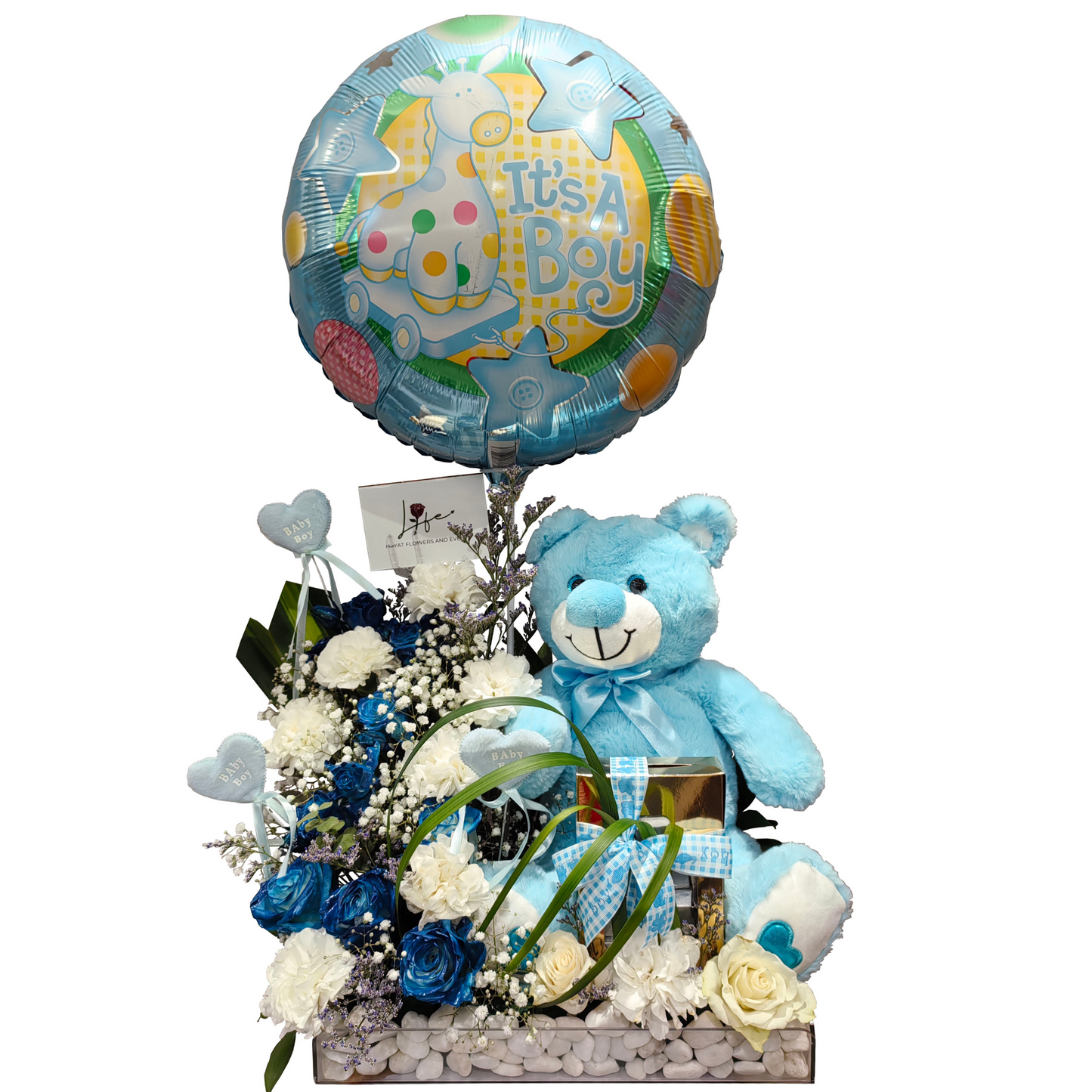 Gift arrangement for baby boy with blue teddy bear, It’s a Boy balloon, white carnations, blue roses, baby-themed decor, and wrapped gift box in transparent acrylic base with white pebbles.