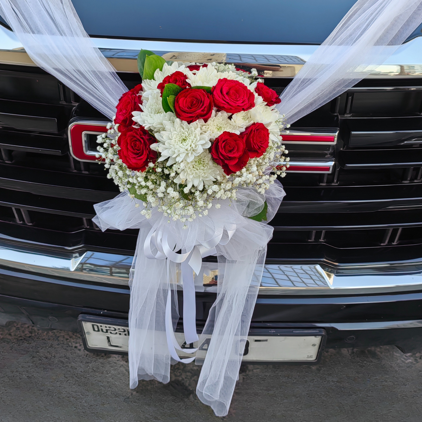 Hayat Flower's PURE LOVE bouquet of red and white flowers with foliage on a GMC car grille.