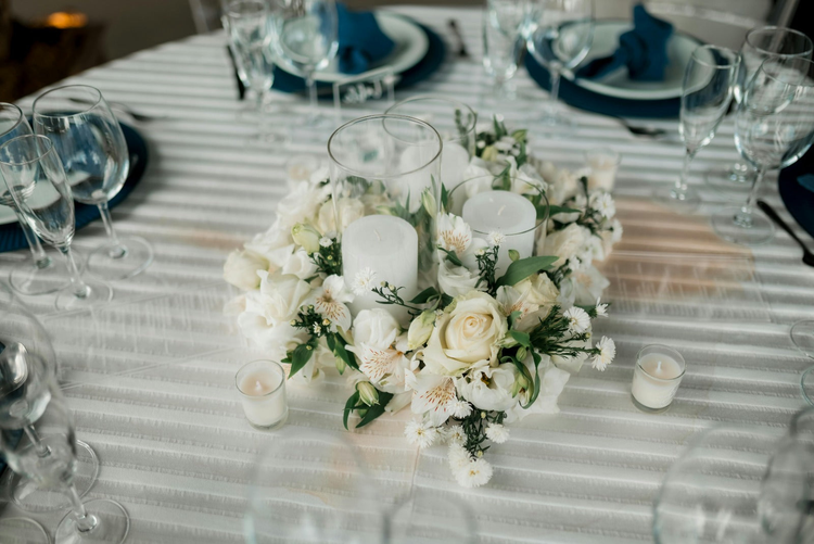 Wedding or event centerpiece with white blooms, greens, and pillar candles