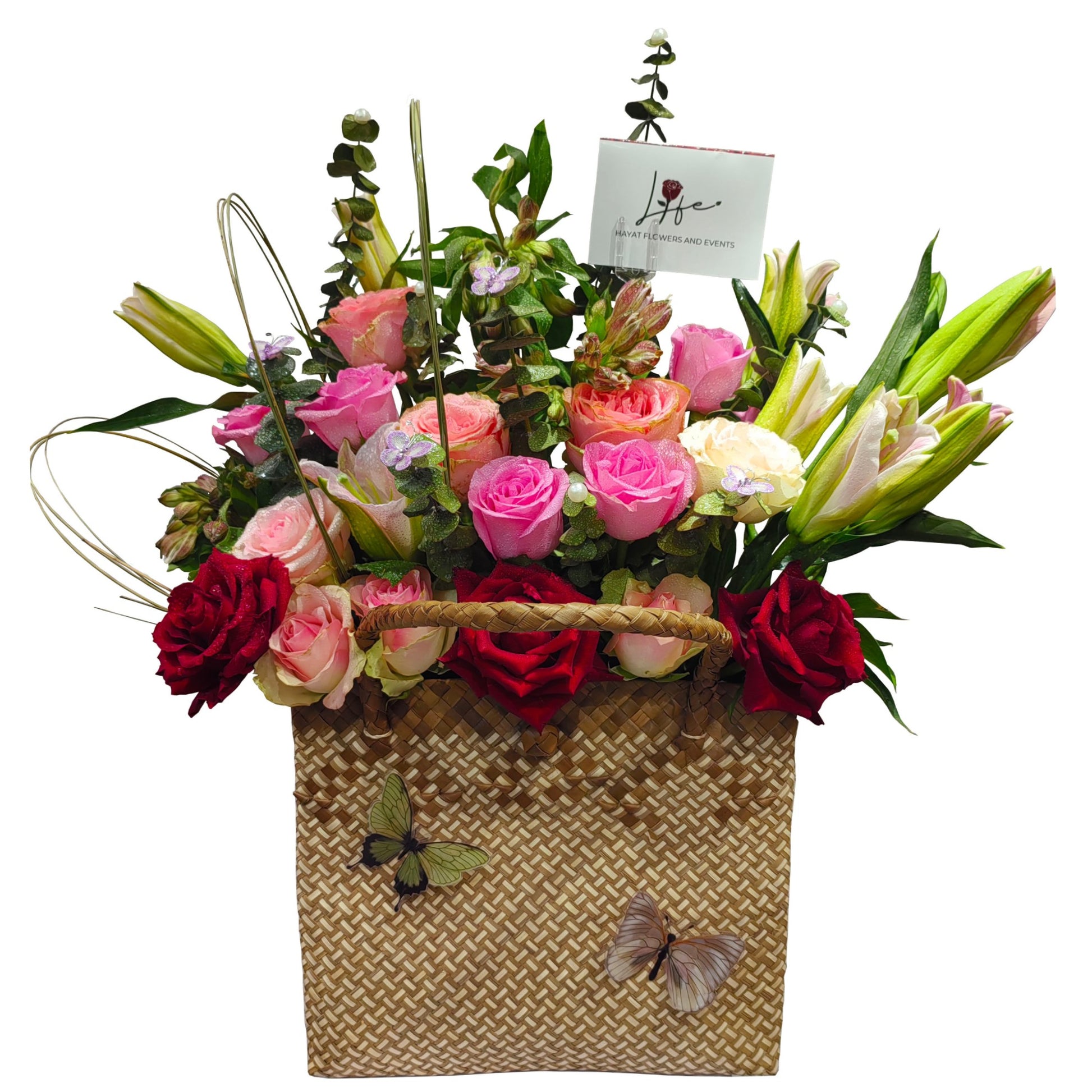 Floral arrangement in a woven basket with pink, red, and white roses and pink lilies, accented with eucalyptus baby blue and steel grasses.