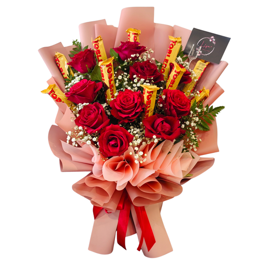 A romantic bouquet of 10 red roses and 10 Toblerone chocolate bars, accented with white gypsophila and fern leaves, wrapped in elegant pink paper and tied with a red ribbon from Hayat Flowers & Events.