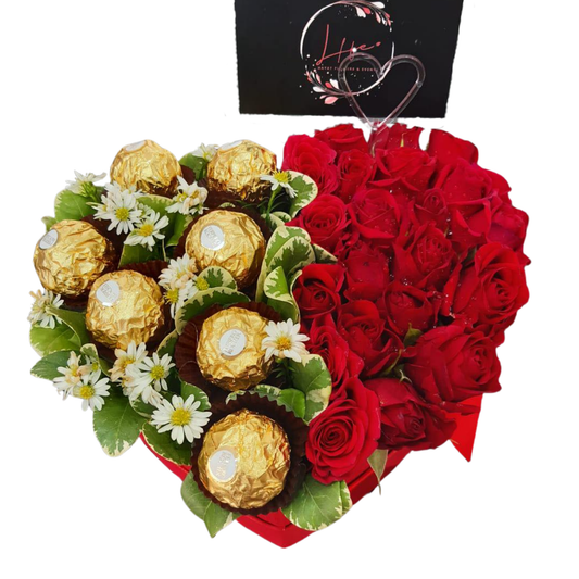 Heart-shaped red flower box featuring fresh red roses, and the opposite half is filled with 7 Ferrero Rocher chocolates and delicate camomile, styled with foliage for romantic gifting.