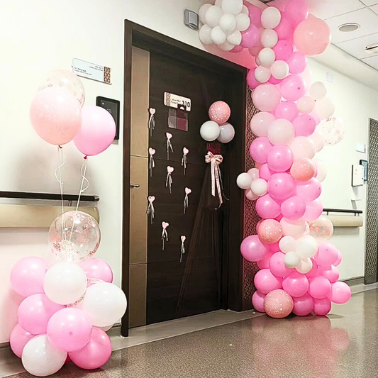 Decorative pink pastel balloon arch and decorations outside a maternity room door.