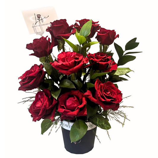 RED ROSE SPLENDOR Arrangement of lovely roses, single ruscus and grass fountain underneath for a natural rose garden displayed in a black pot.
